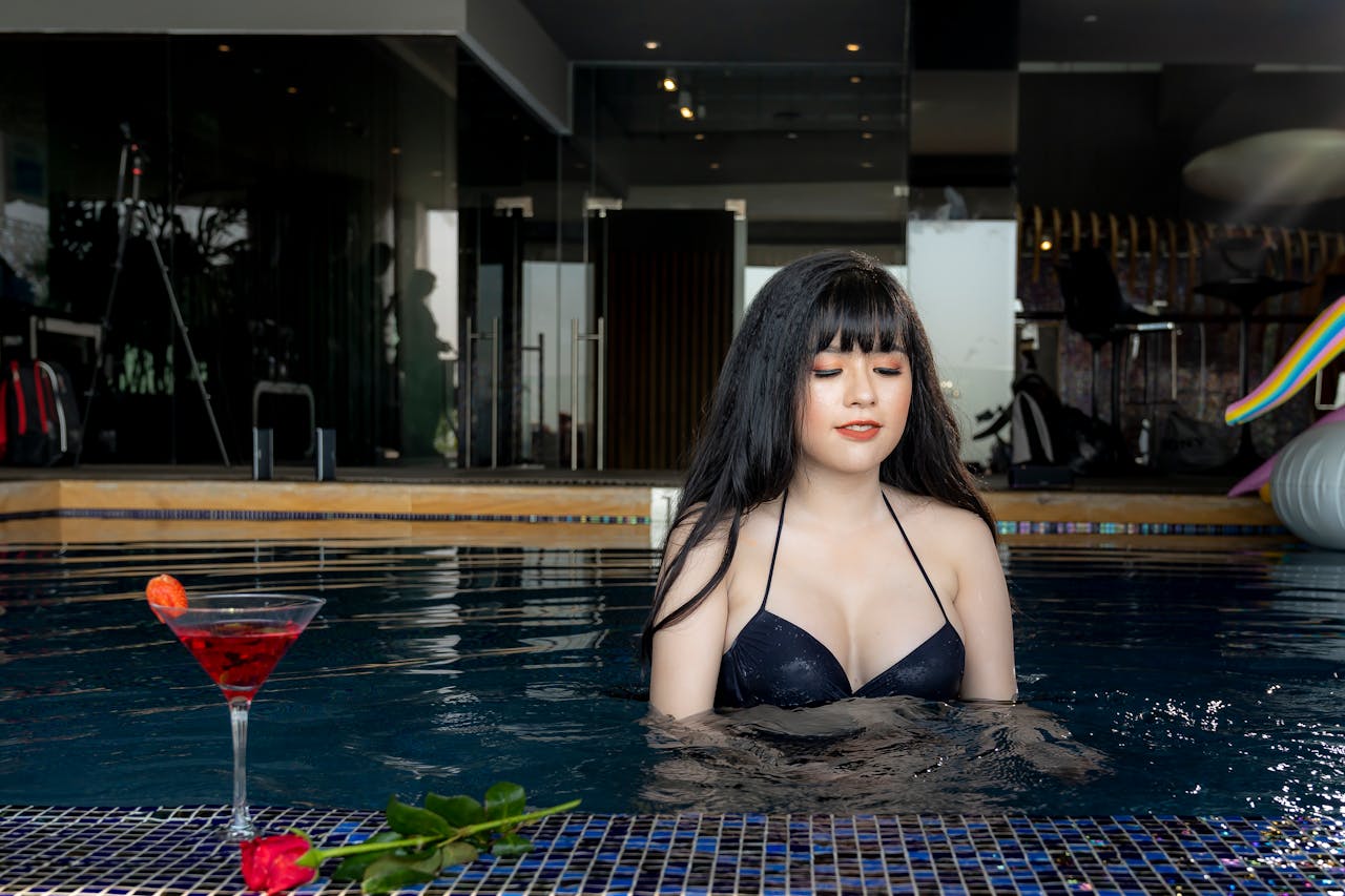 Facilities Woman enjoying a relaxing moment in an indoor swimming pool with a cocktail and rose nearby.