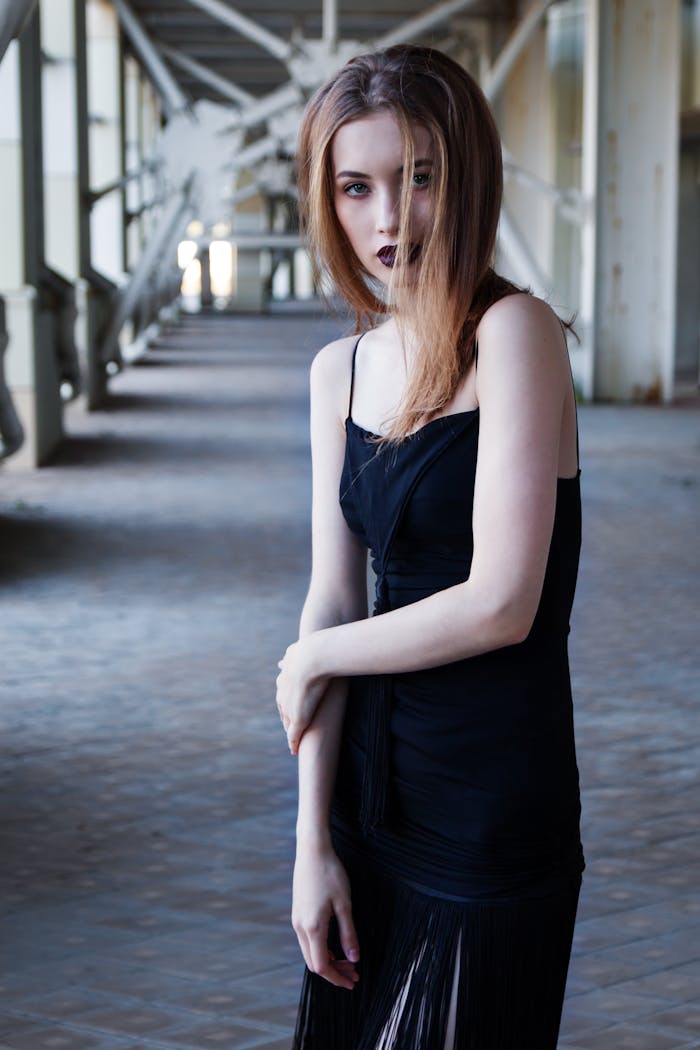 A stylish young woman in a black dress posing confidently in an industrial setting.